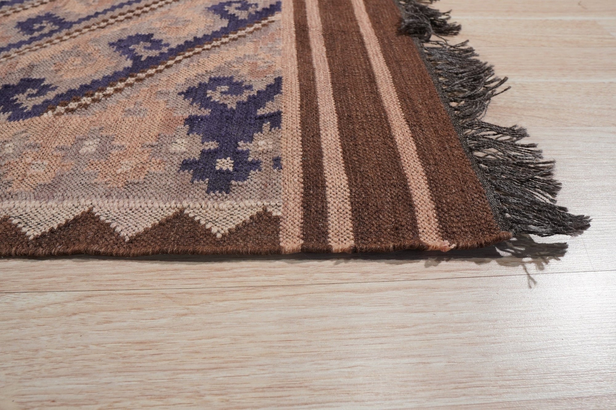 Penelope Jade Brown Flatweave Wool Rug, blending earthy browns and subtle jade tones, lies beneath a modern living space. The flatweave wool construction adds texture and warmth to the light wood flooring, creating a cozy and inviting atmosphere.