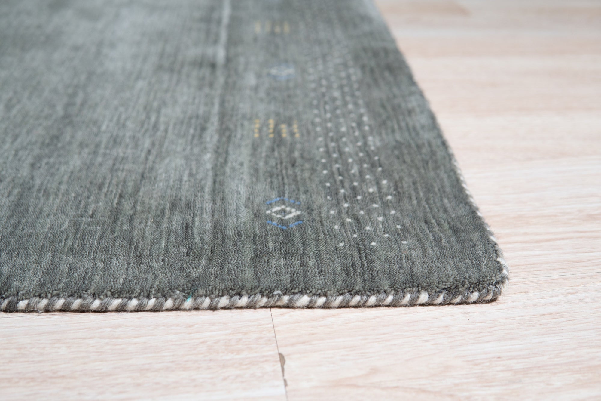 Freya Gabbeh Gray Handmade Wool Rug, a muted gray wool rug with a minimalist Gabbeh design, partially seen beneath a mid-century modern style living room setup.