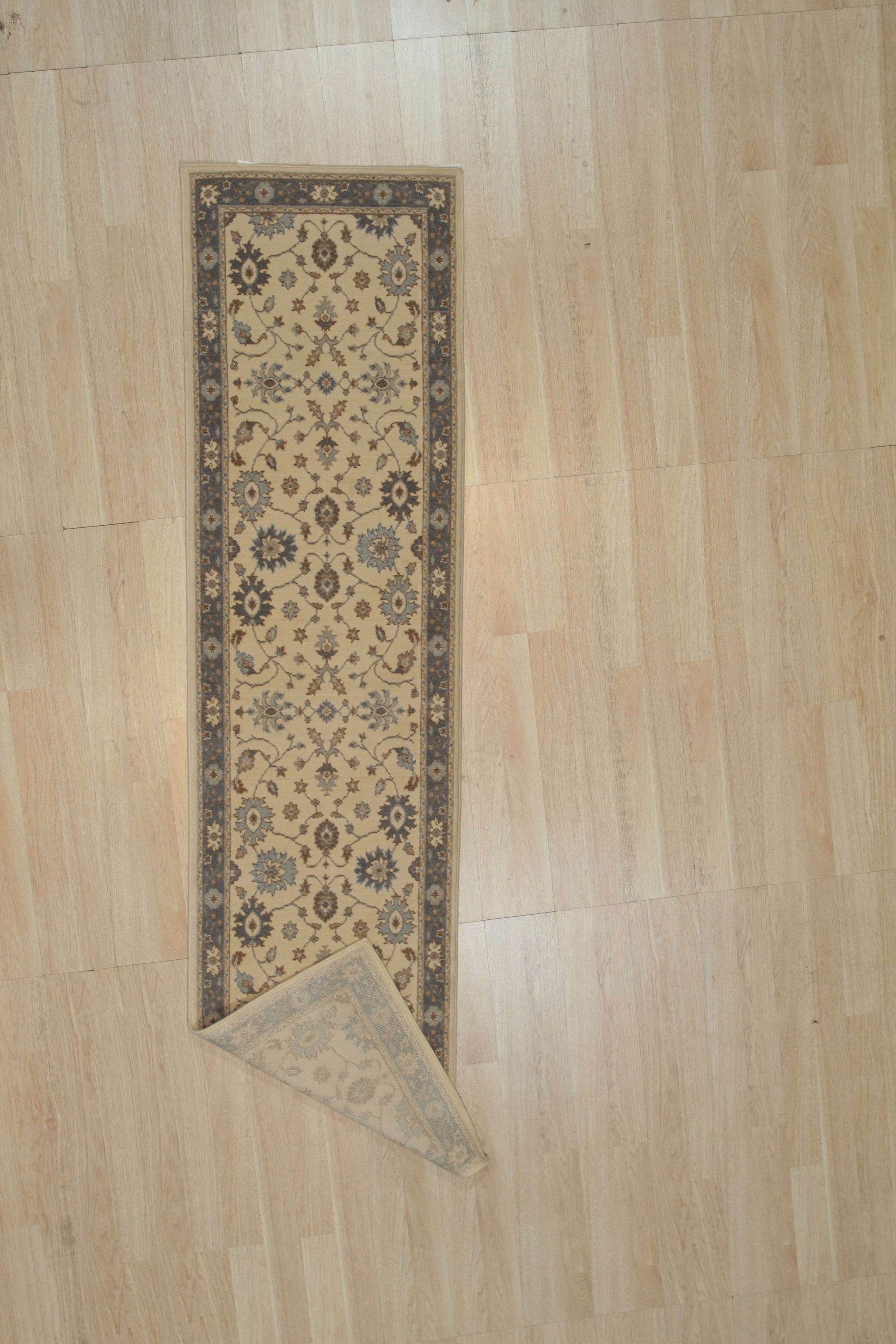 Ivory and slate blue Oushak wool runner rug with a corner folded back to show the hand knotted pile and backing