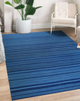 Trara Penelope Blue Flatweave Wool Rug, a textured flatweave with a geometric diamond pattern in shades of blue and cream, displayed in a bright, modern living room setting.