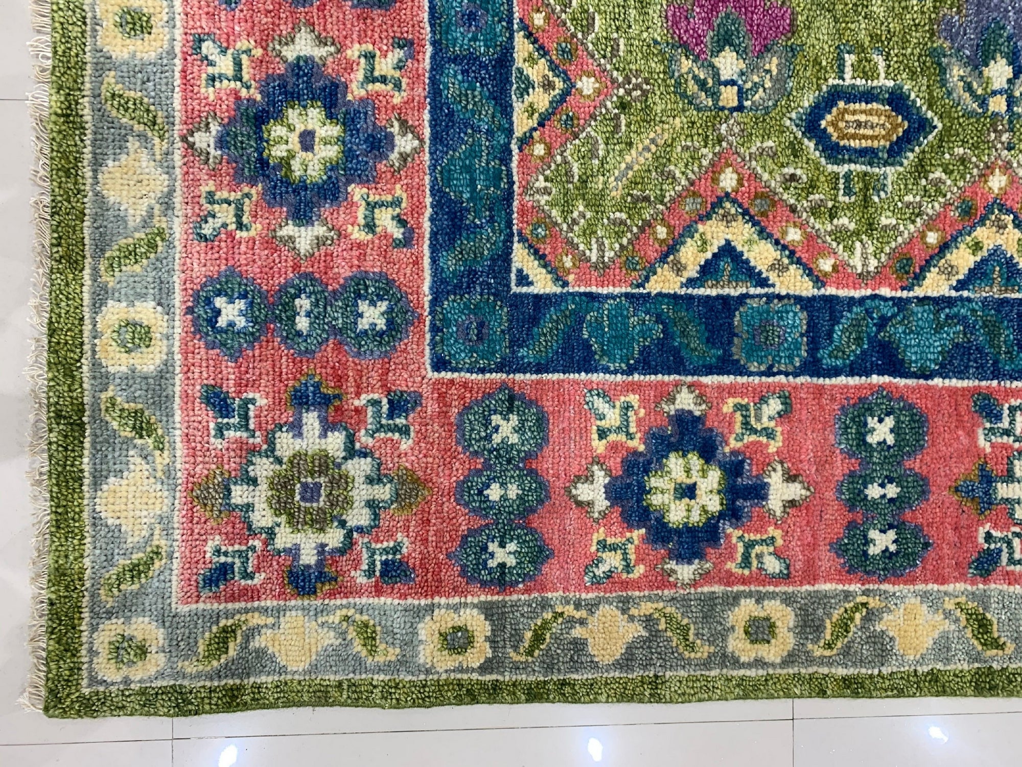 High-pile rug corner showing vivid geometric designs in pink, blue, lime green, and teal on white tile.