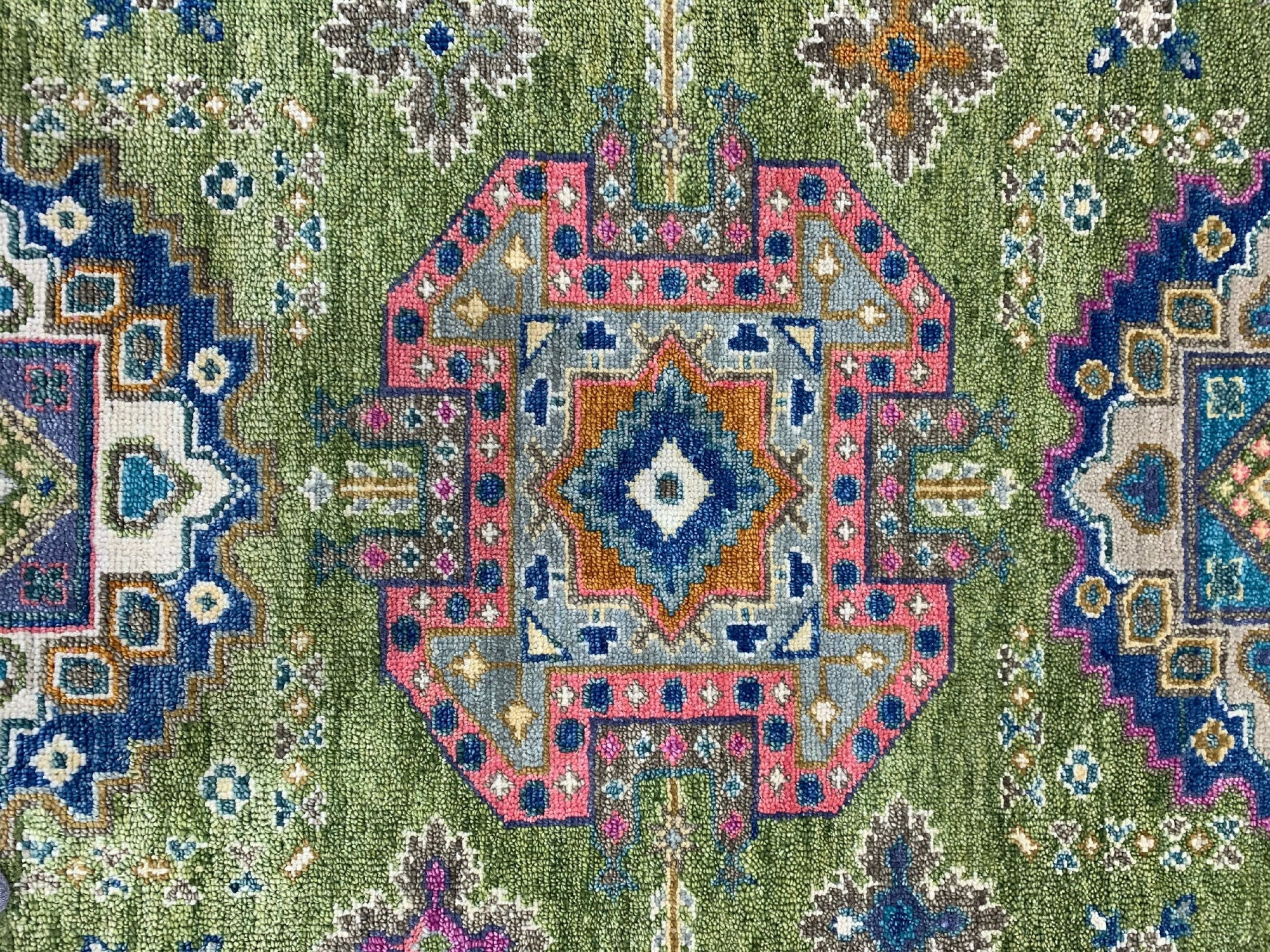 Green textured rug detail with a geometric medallion pattern in pink, blue, gray, and rust colors.